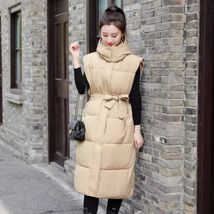 Doudoune longue sans manche avec capuche beige portée ceinture nouée à la taille, sur un haut noir